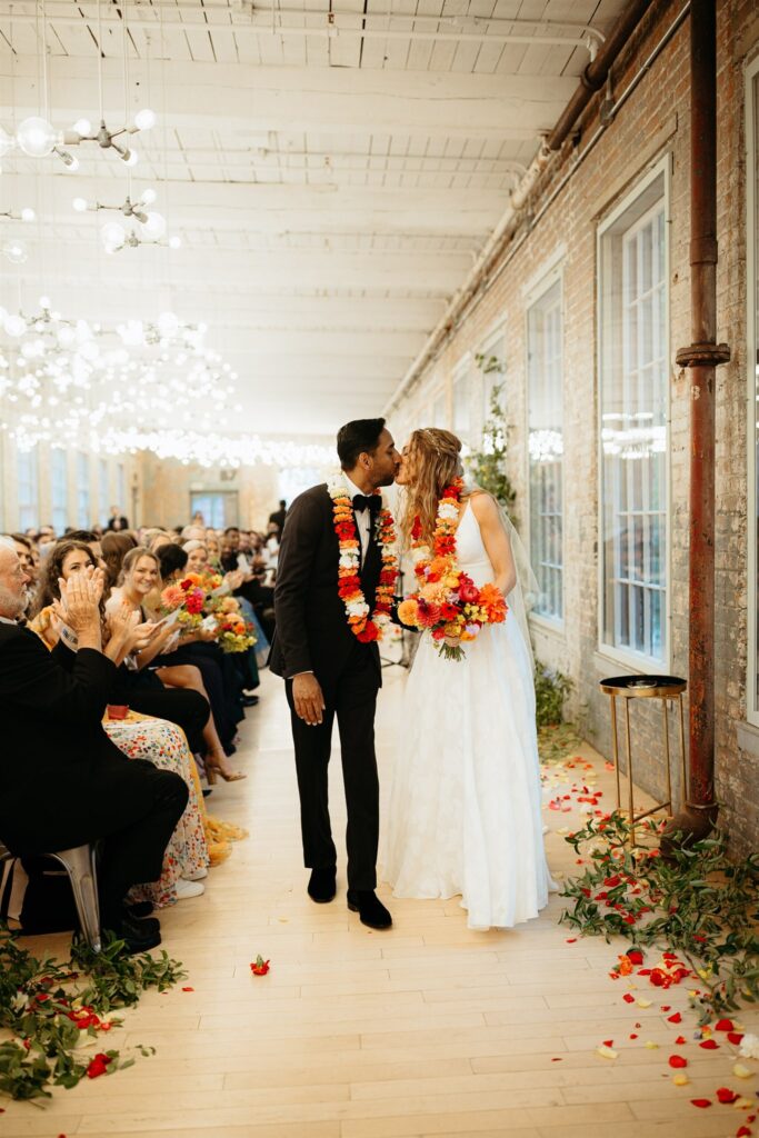 bride and groom kiss while wearing florals during wedding recessional